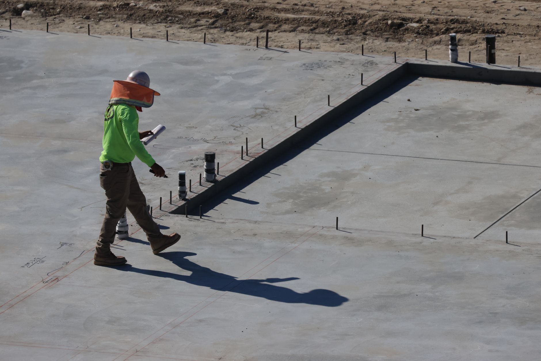 Site worker inspecting a large poured concrete raft foundation slab