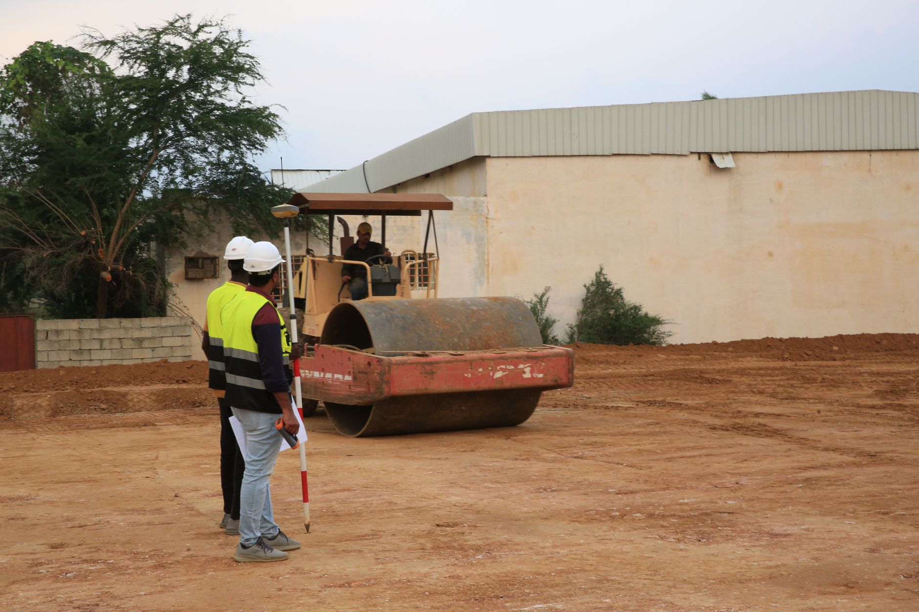 Worker guiding a road roller compacting a soil layer on site
